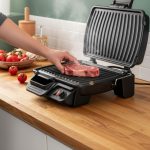 Zijaanzicht van een geopende Tefal Grill Ultracompact GC3058 met dikke grillplaten en een biefstuk op het hete oppervlak.